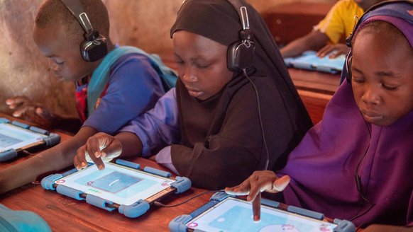 Three children in Chad on with headphones and tables using Can't Wait to Learn - War Child's education app