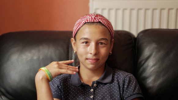 Roda (12) sitting on a couch, with a red headband smiling at the camera